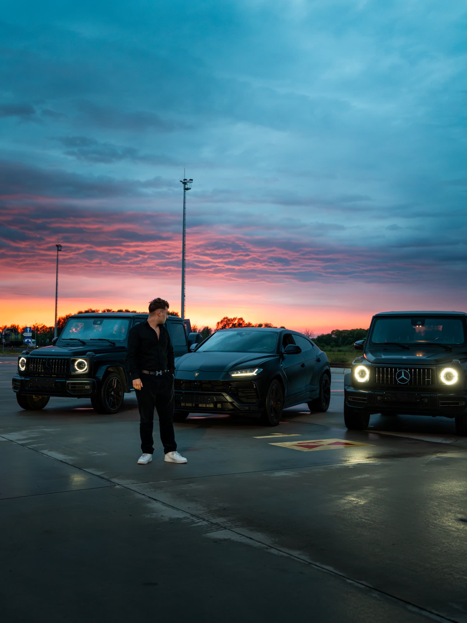 Gerox obok czarnego Lamborghini Urus i dwóch Mercedesów G 63 o zachodzie słońca